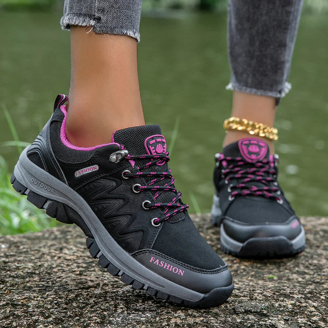 Black and pink outdoor fashion sneakers with gray soles worn with cropped jeans near water