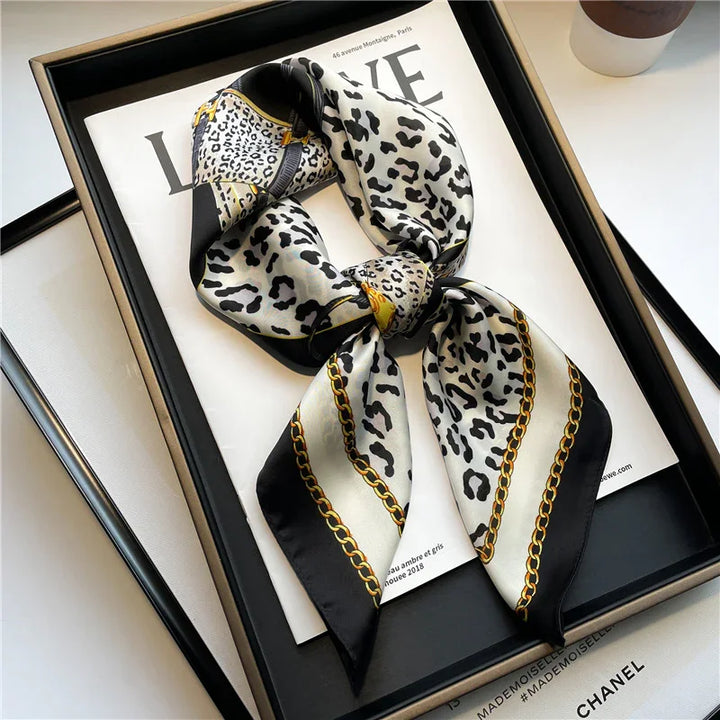 Silk leopard print scarf with gold chain pattern displayed on a fashion magazine in a black tray