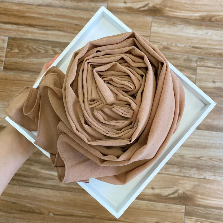 Hand holding white box with neatly folded camel brown chiffon fabric scarf on wooden floor