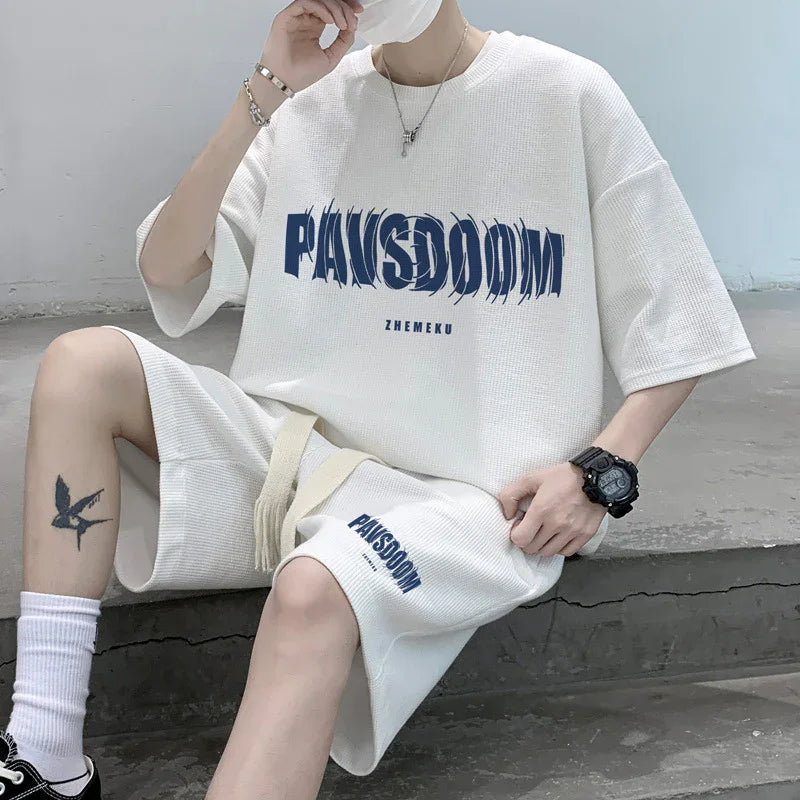 Person wearing white short sleeve shirt and shorts with blue PANSDOOM print and tattoo on leg sitting on concrete steps