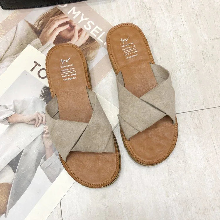 Pair of tan leather sandals with beige crossed fabric straps on tile floor and magazines