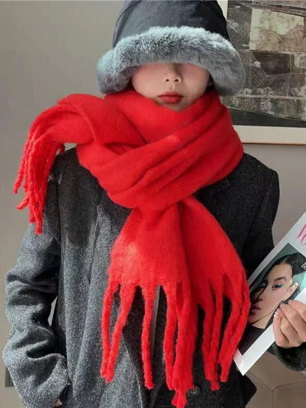 Person wearing a dark gray coat, black fur hat, and thick bright red scarf indoors holding a magazine