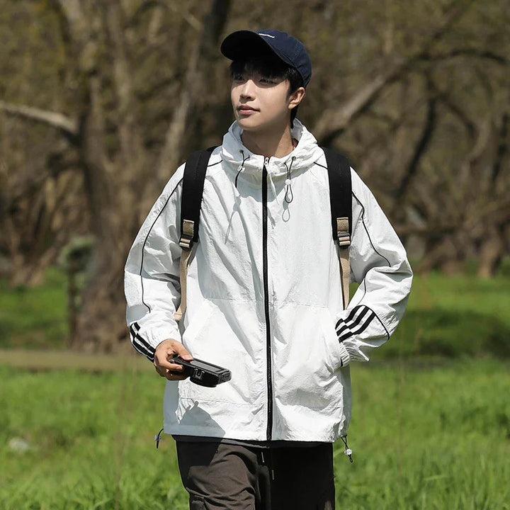 Young man wearing a white hooded jacket with black stripes, black cap, and backpack outdoors
