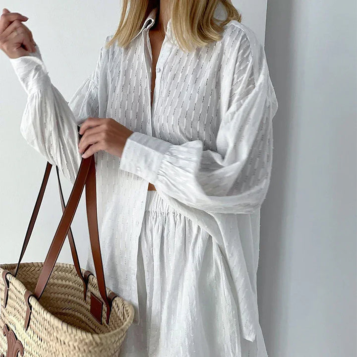 Woman wearing a textured white button-up shirt and skirt holding a woven straw tote bag with leather straps