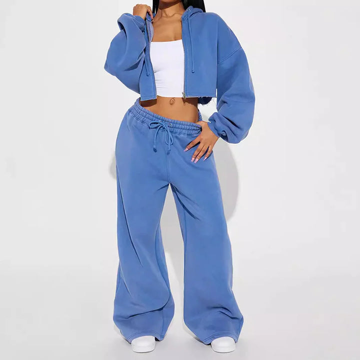 Woman wearing blue cropped hoodie and wide-leg sweatpants with white sneakers on white background