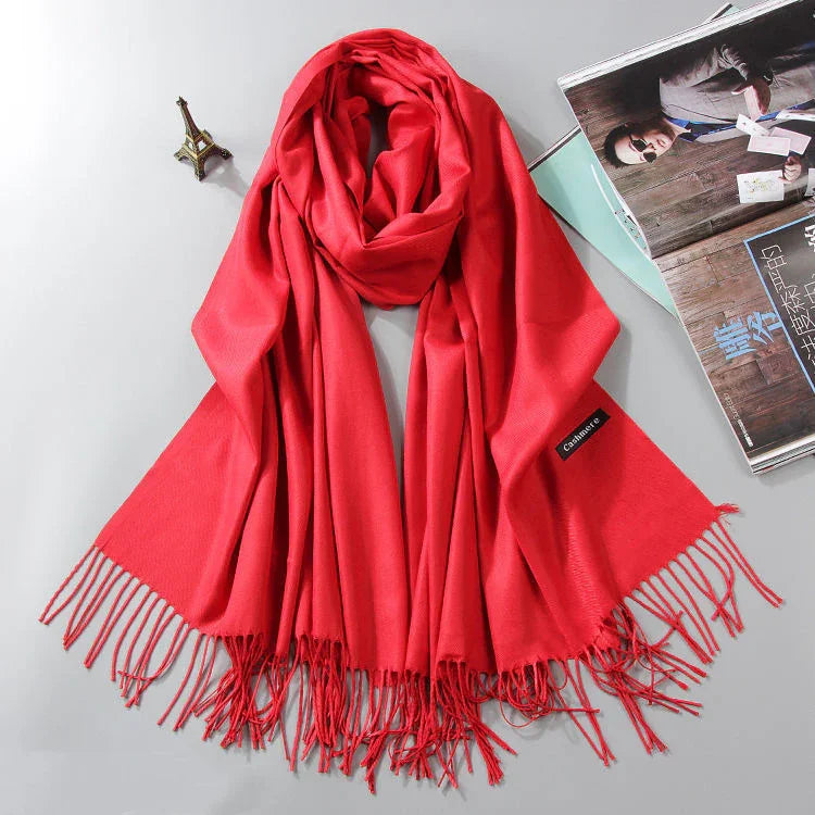 Bright red cashmere scarf with fringes laid on light gray surface next to miniature Eiffel Tower and open magazine