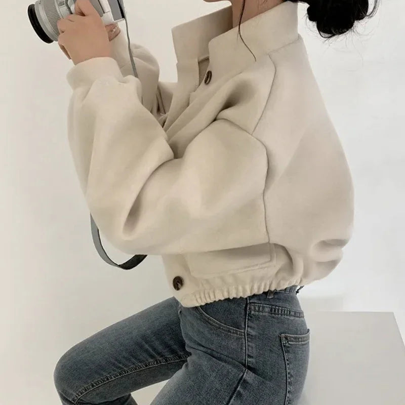 Woman in beige cropped jacket and blue jeans holding a camera in minimalist setting