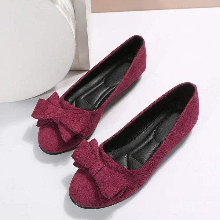 Women’s burgundy suede flat shoes with large decorative bows and cushioned insoles