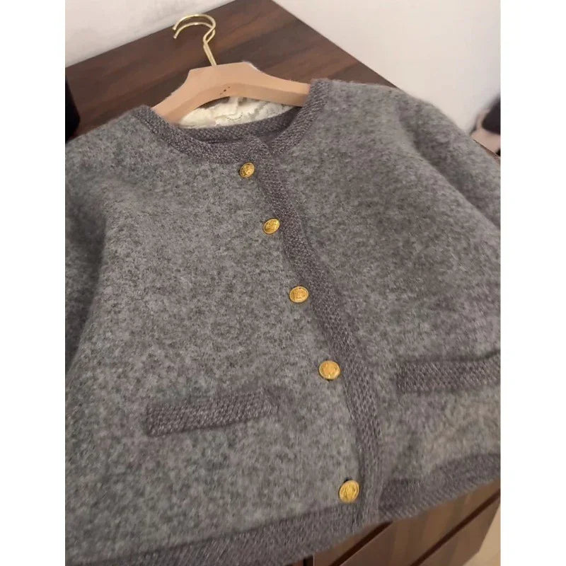 Gray wool cardigan with gold buttons on wooden hanger on dark wood surface