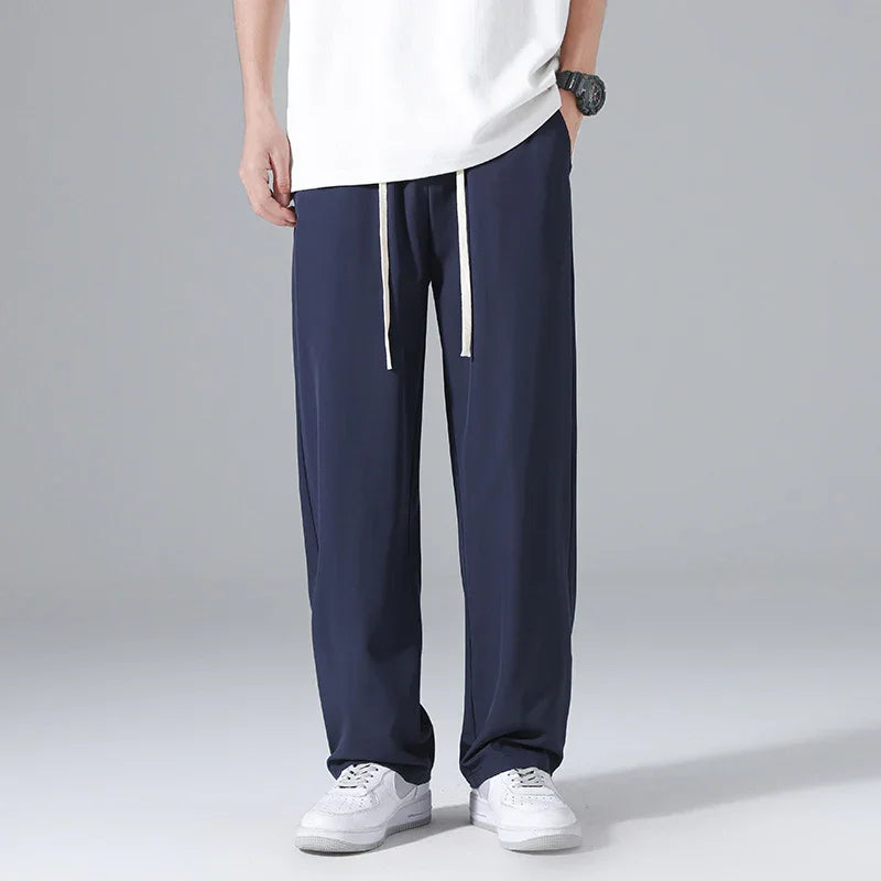 Men's navy blue casual pants with white drawstrings, paired with white sneakers on gray background