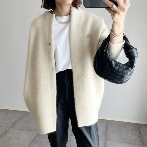 Woman wearing cream oversized cardigan, white t-shirt, black pants, holding black woven handbag