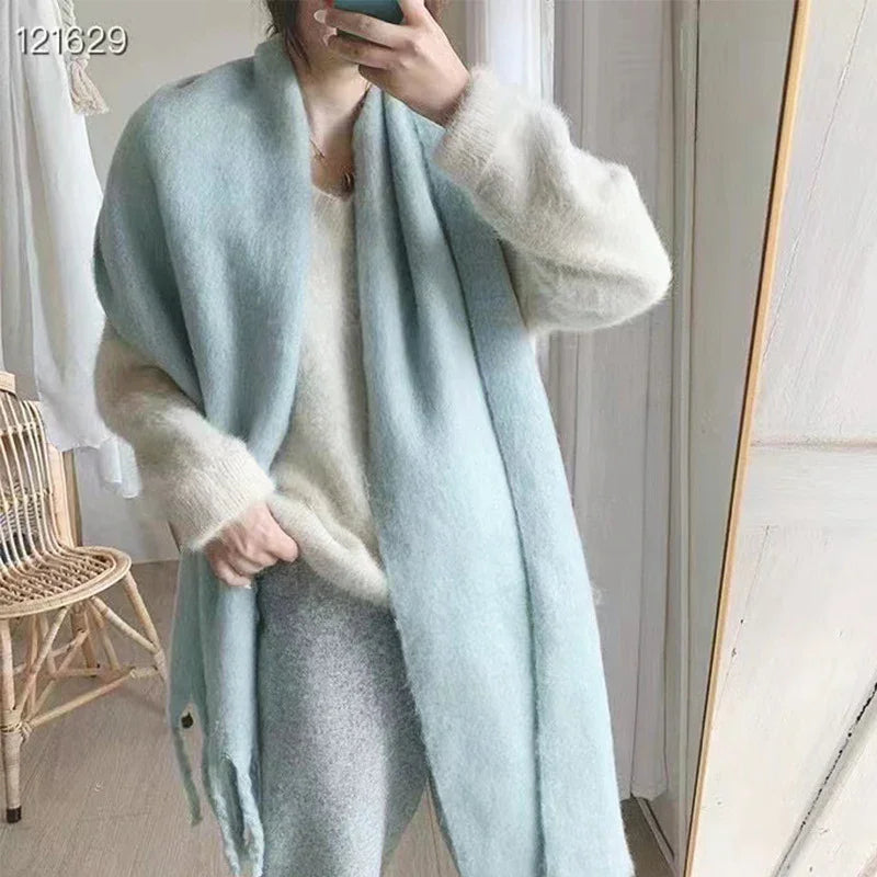 Woman wearing cozy light blue scarf and cream sweater taking mirror selfie in minimal room