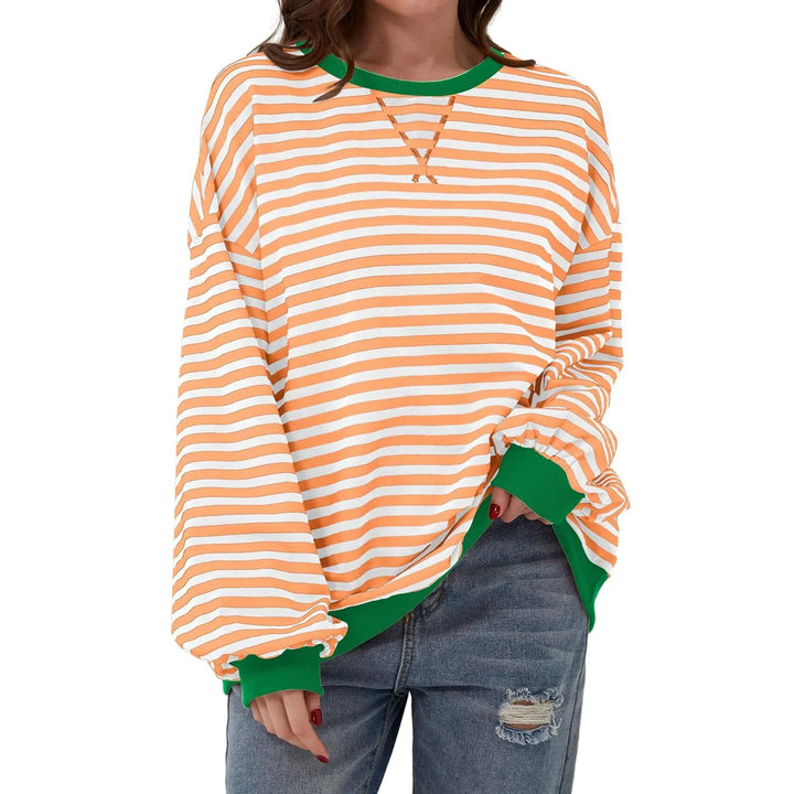 Woman wearing orange and white striped long sleeve sweatshirt with green cuffs and collar, paired with ripped jeans
