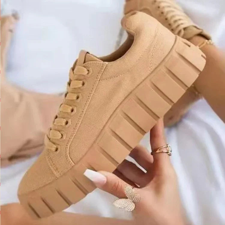Beige platform sneakers with chunky soles held by a hand wearing butterfly and gold rings