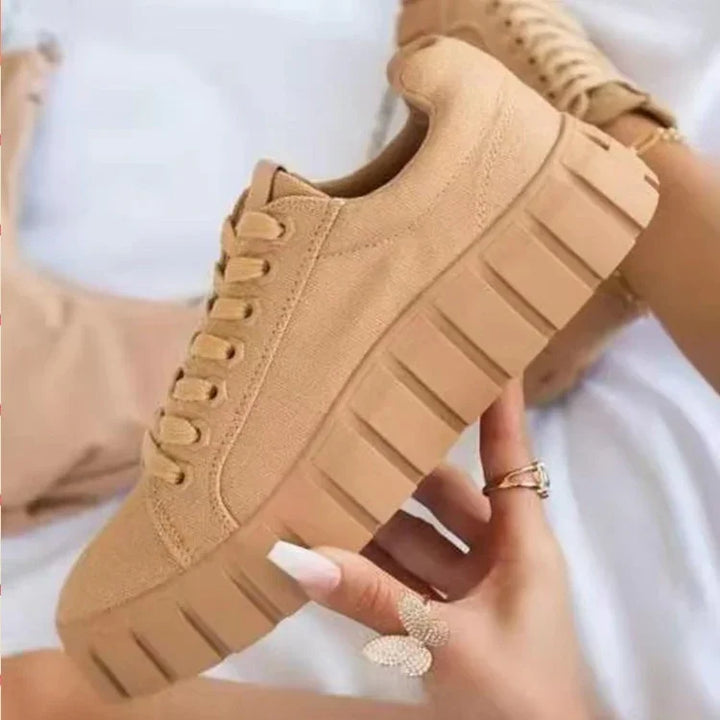 Beige platform sneakers with chunky soles held by a hand wearing butterfly and gold rings