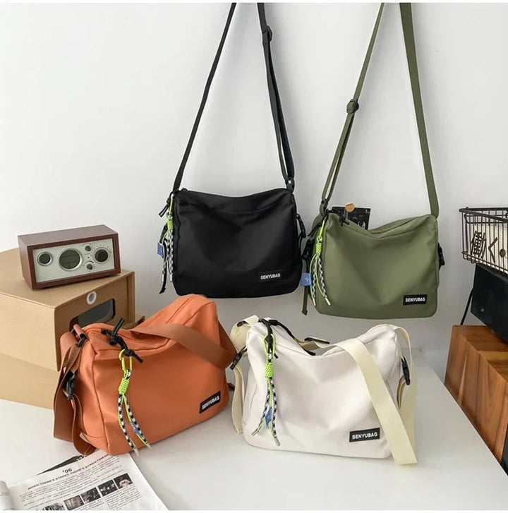 Four stylish SENYUBAG shoulder bags in black, green, orange, and white displayed on a white table and hanging on a wall