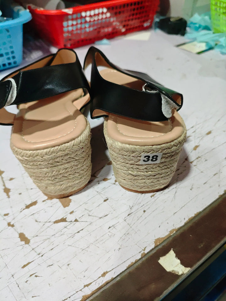Pair of black leather wedge sandals with rope-covered heels on worn white wooden surface