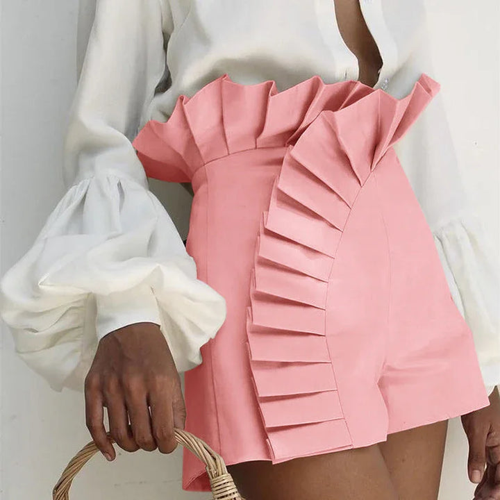 Woman wearing pink high-waisted shorts with pleated ruffle detail and white puff sleeve blouse holding wicker basket