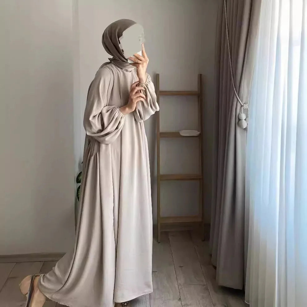 Woman in beige abaya and hijab taking mirror selfie in minimalistic room with wooden floor and ladder