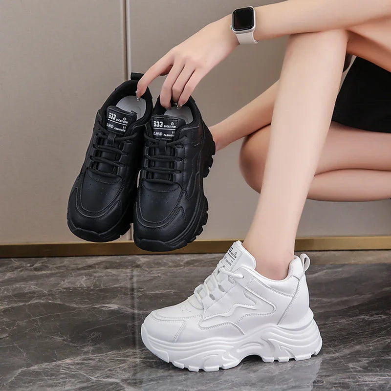Person holding black chunky sneakers and wearing white platform athletic shoes on marble floor