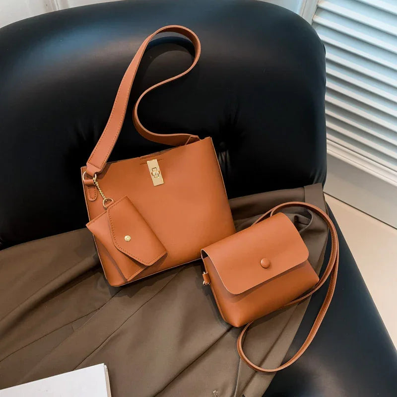 Two tan leather crossbody bags with a small coin purse on a black leather chair and brown fabric