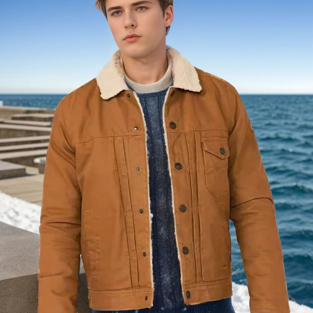 Young man wearing brown shearling collar jacket and blue sweater near ocean pier under clear sky