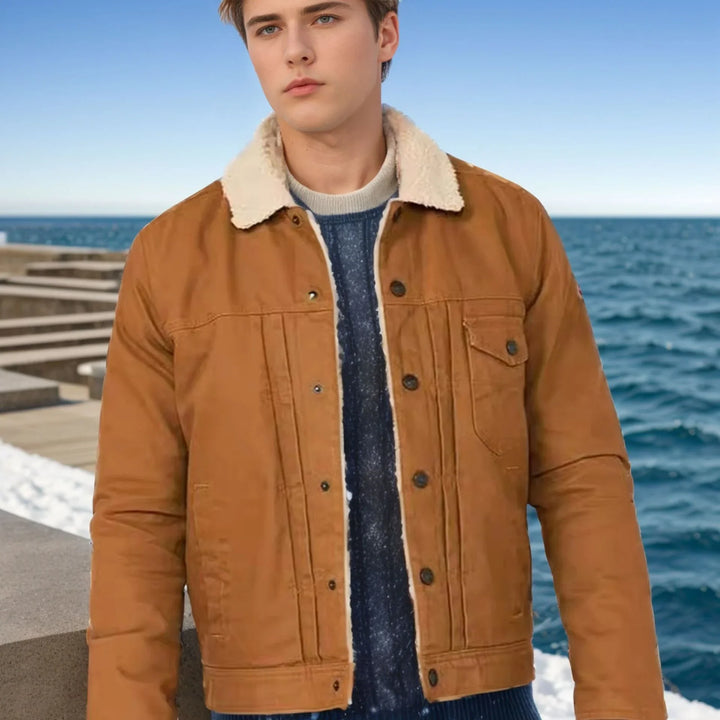 Young man wearing brown shearling collar jacket and blue sweater near ocean pier under clear sky