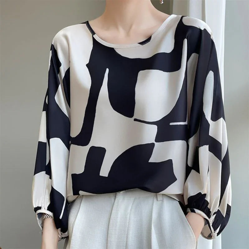 Woman wearing a loose black and white abstract print blouse with 3/4 sleeves and white pants