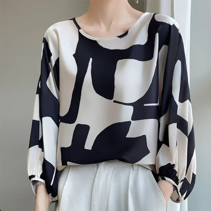 Woman wearing a loose black and white abstract print blouse with 3/4 sleeves and white pants