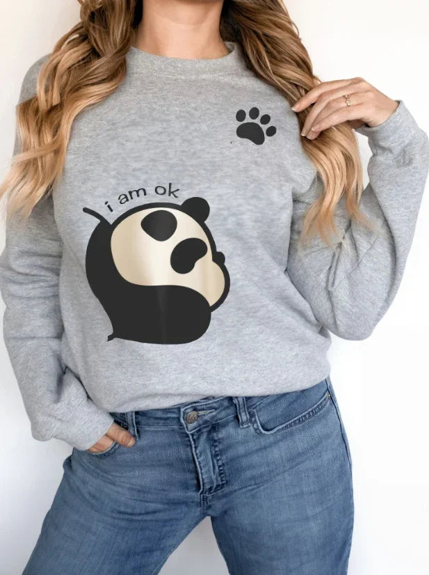 Woman wearing grey sweatshirt with panda graphic and text 'i am ok' and a black paw print design