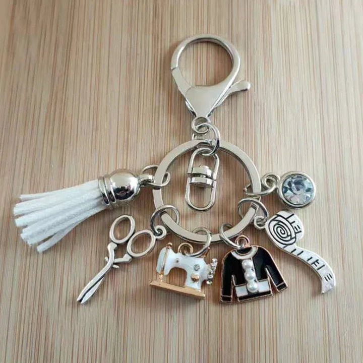 Sewing-themed keychain with white tassel, scissors, sewing machine, jacket, measuring tape, and rhinestone charm on wood