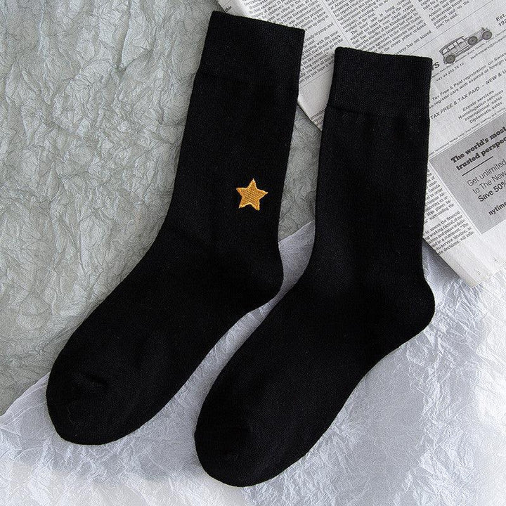 Pair of black socks with a yellow star embroidery on one leg, laid on textured surface with newspaper