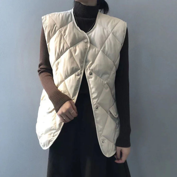 Person wearing beige quilted vest over brown ribbed turtleneck sweater against gray wall