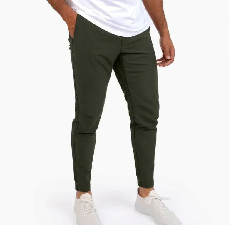 Man wearing slim-fit dark green jogger pants and white sneakers on white background