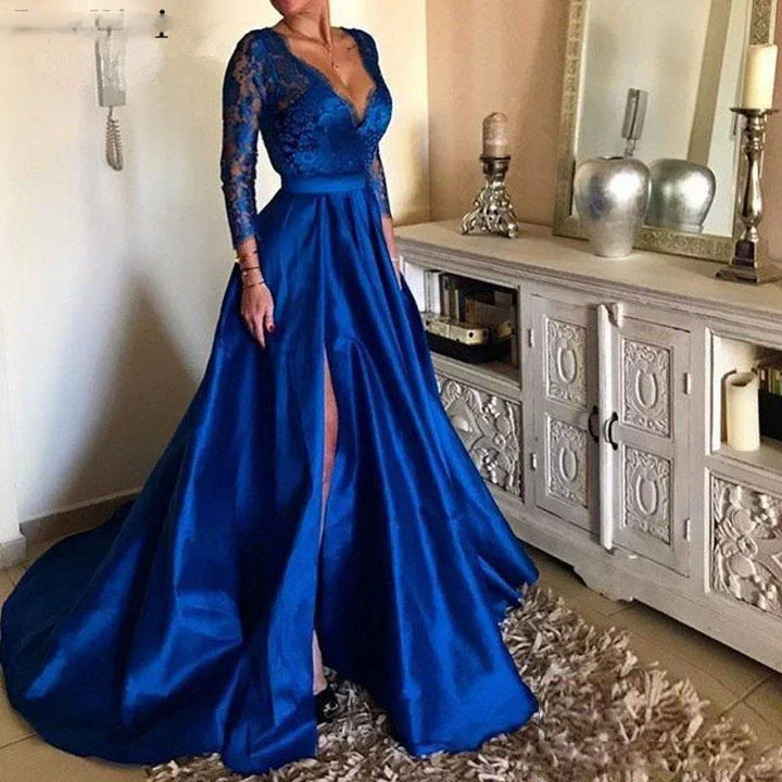 Woman wearing elegant royal blue satin evening gown with lace long sleeves and thigh-high slit standing indoors