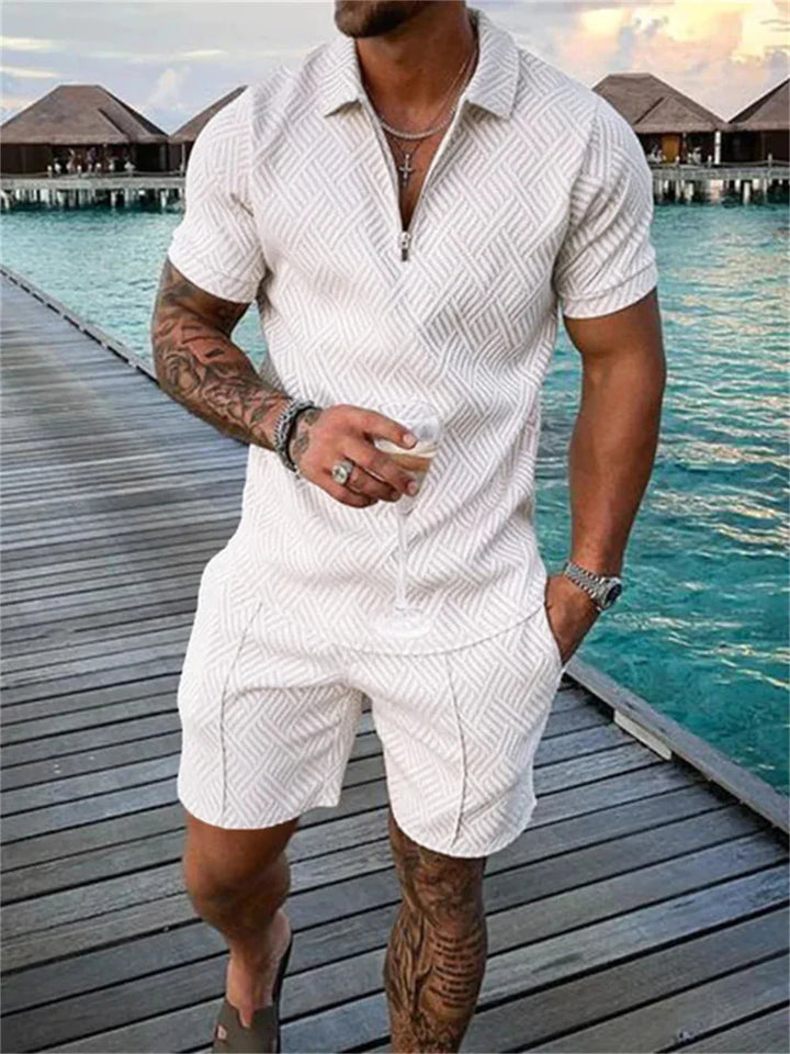 Man in white textured short-sleeve shirt and shorts holding a wine glass on a wooden pier by turquoise water