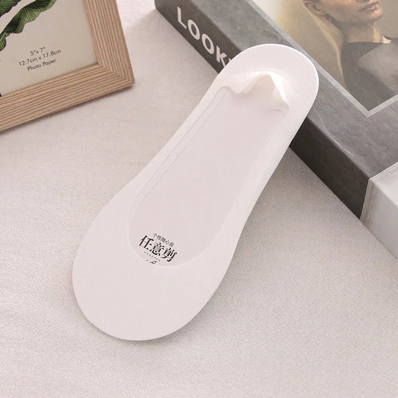 White no-show liner sock displayed on beige surface next to photo frame and book