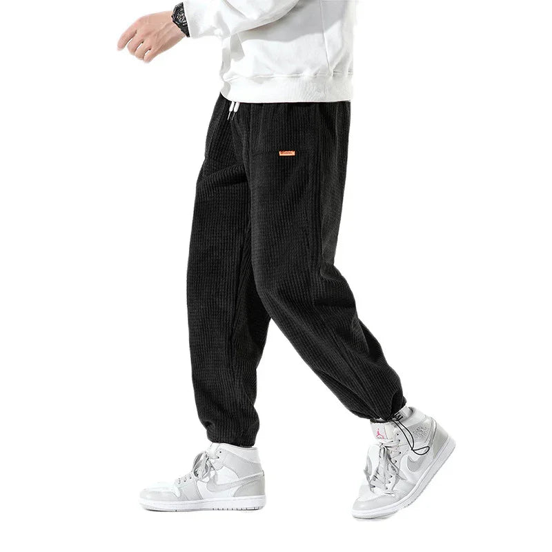 Person wearing black corduroy jogger pants with elastic cuffs and white high-top sneakers
