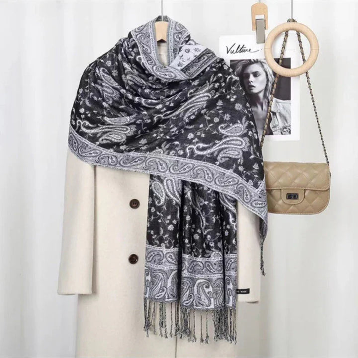 Black and white paisley patterned scarf draped over beige buttoned coat with quilted tan handbag