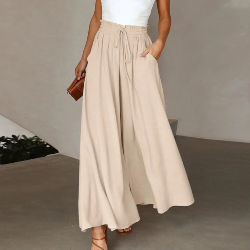 Woman wearing beige wide-leg pants with drawstring waist and white top holding brown clutch