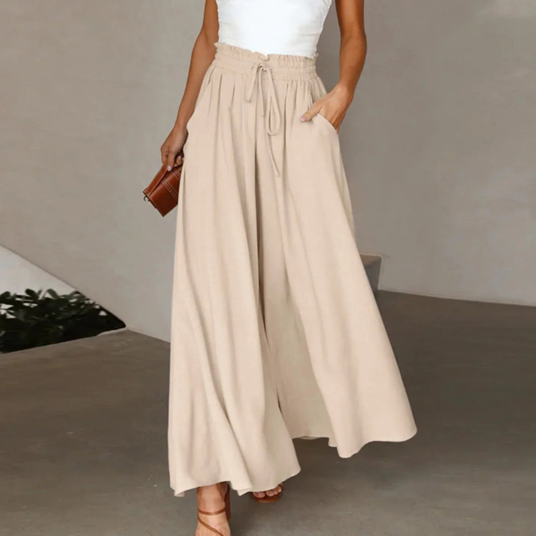 Woman wearing beige wide-leg pants with drawstring waist and white top holding brown clutch