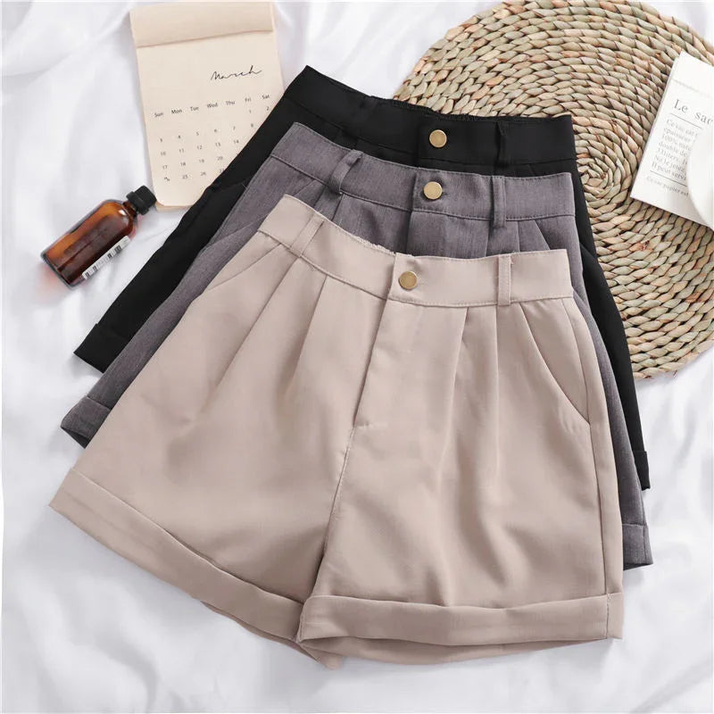 Three pleated high-waist shorts in beige, gray, and black with button closures on white fabric