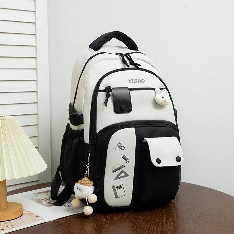White and black YIBAO school backpack with bunny charm and cute keychain on wooden table
