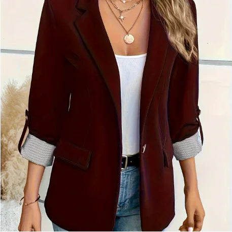 Woman wearing burgundy blazer with rolled sleeves, white top, layered gold necklaces, and jeans