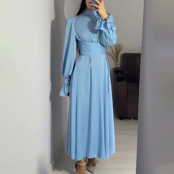 Woman wearing a light blue long-sleeve maxi dress with puff sleeves and a high waist belt