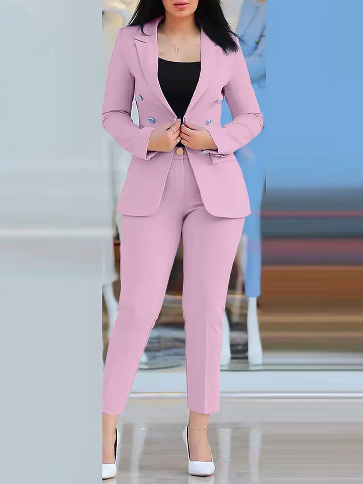 Woman wearing a tailored pink blazer and pants suit with white heels, standing indoors