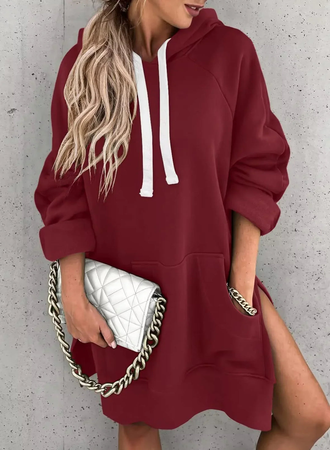 Woman wearing burgundy oversized hoodie with white drawstrings and holding white quilted purse with gold chain