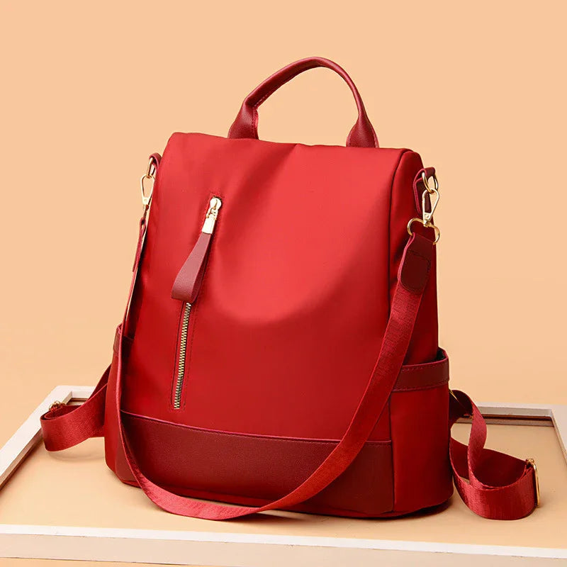 Red stylish backpack with front zipper pocket and adjustable shoulder straps on beige background