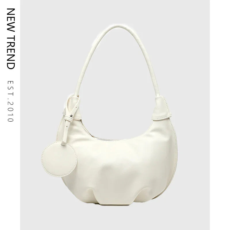 White crescent-shaped leather handbag with round tag and top handle on gray background