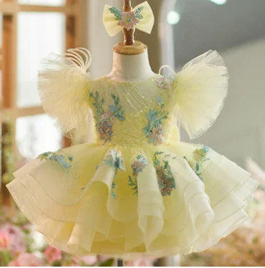Yellow baby dress with tulle sleeves and floral embroidery on a dress form
